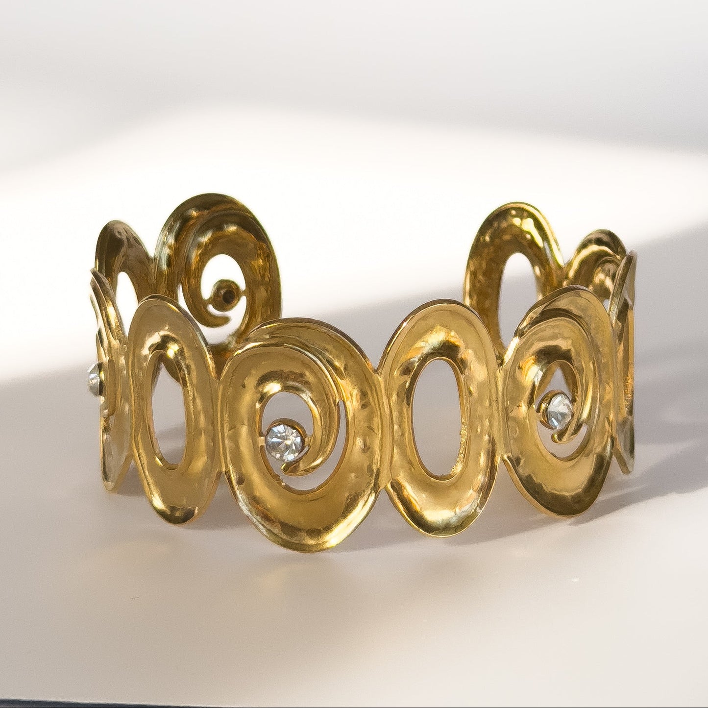 Gold bracelet with intricate design and embedded diamonds on a white background