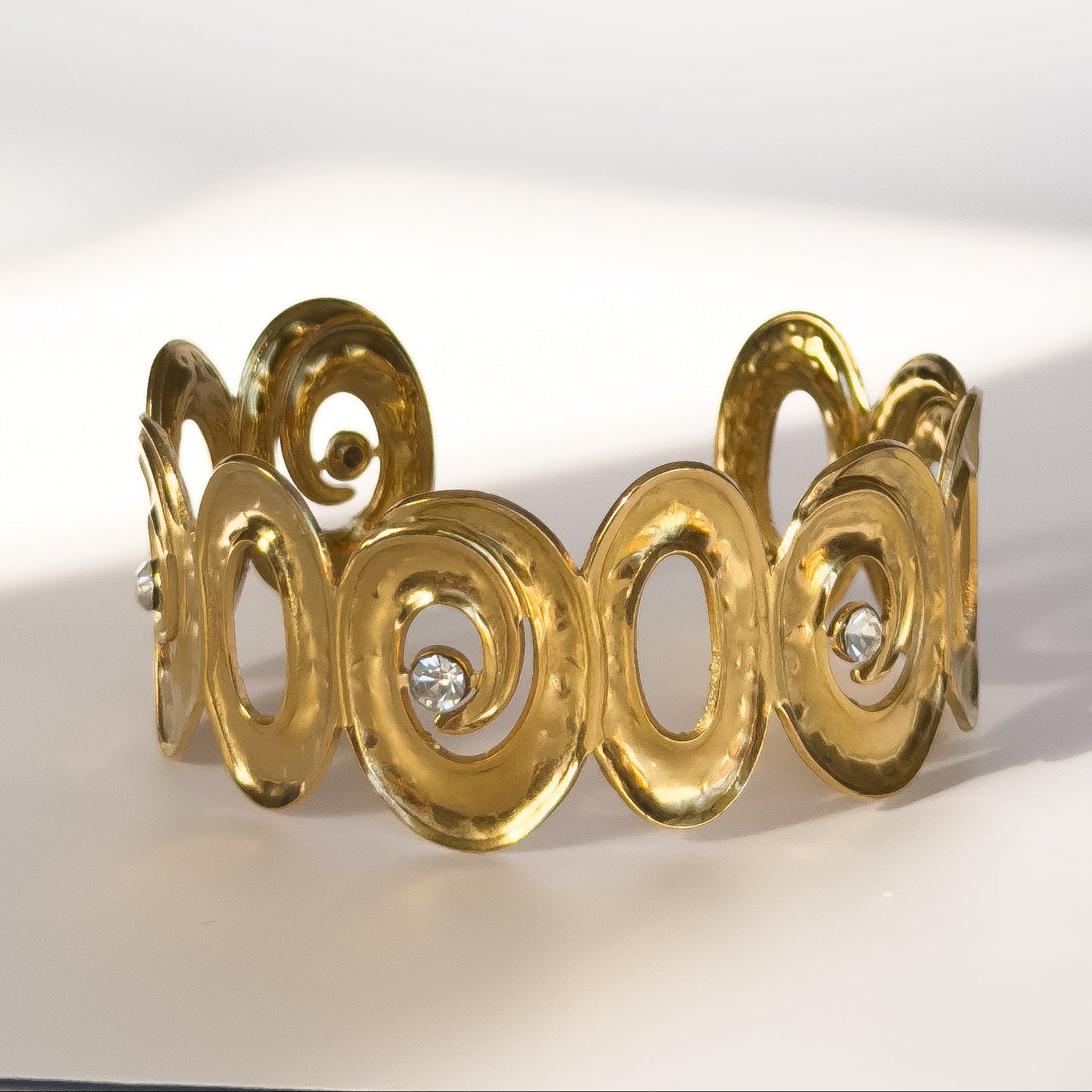 Gold bracelet with intricate design and embedded diamonds on a white background