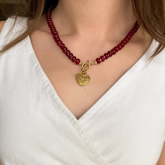 Red beaded necklace with a gold heart pendant on a white top