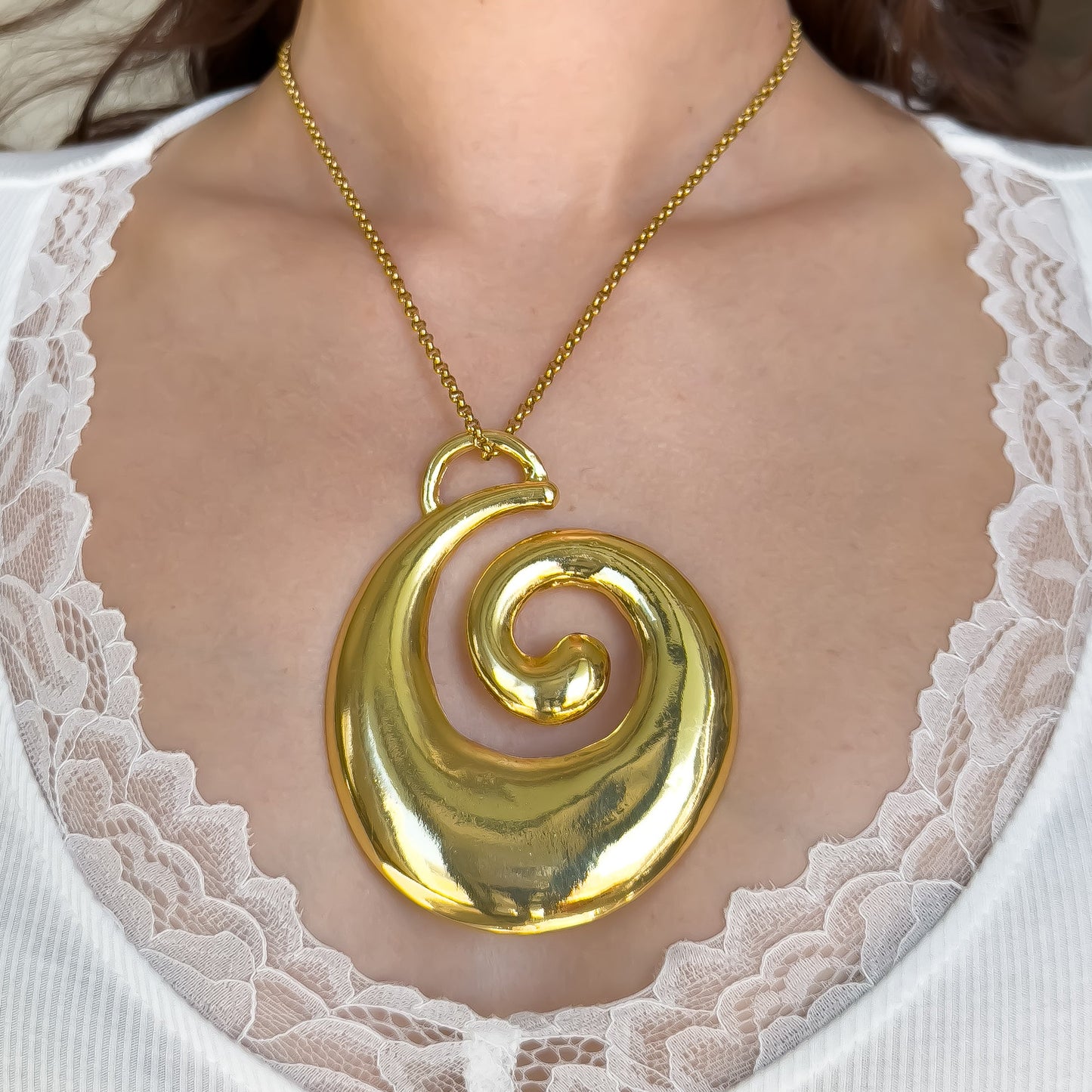 Gold spiral necklace on a person wearing a white lace garment